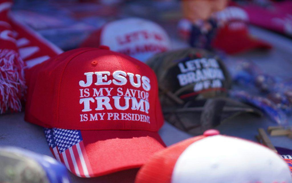 A red hat positioned on a table says 'Jesus is my savior, Trump is my president.