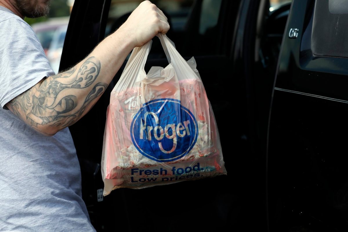 a photo of someone’s tattooed arm as they lift a grocery bag with the word “Kroger” on it into a car