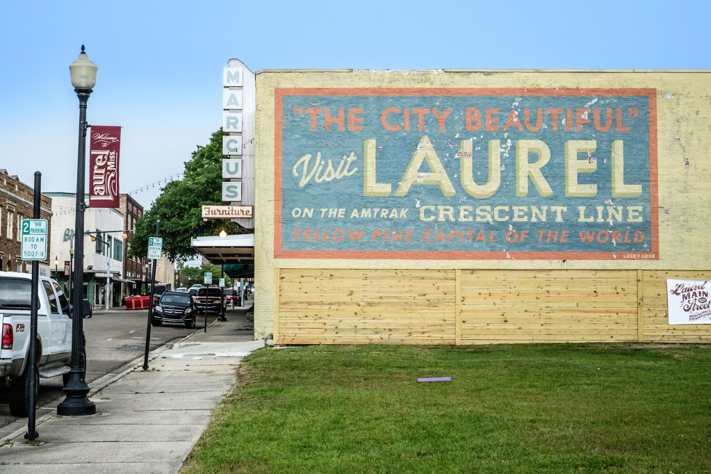 An orange and blue Visit Laurel, Mississippi sign on the side of a building