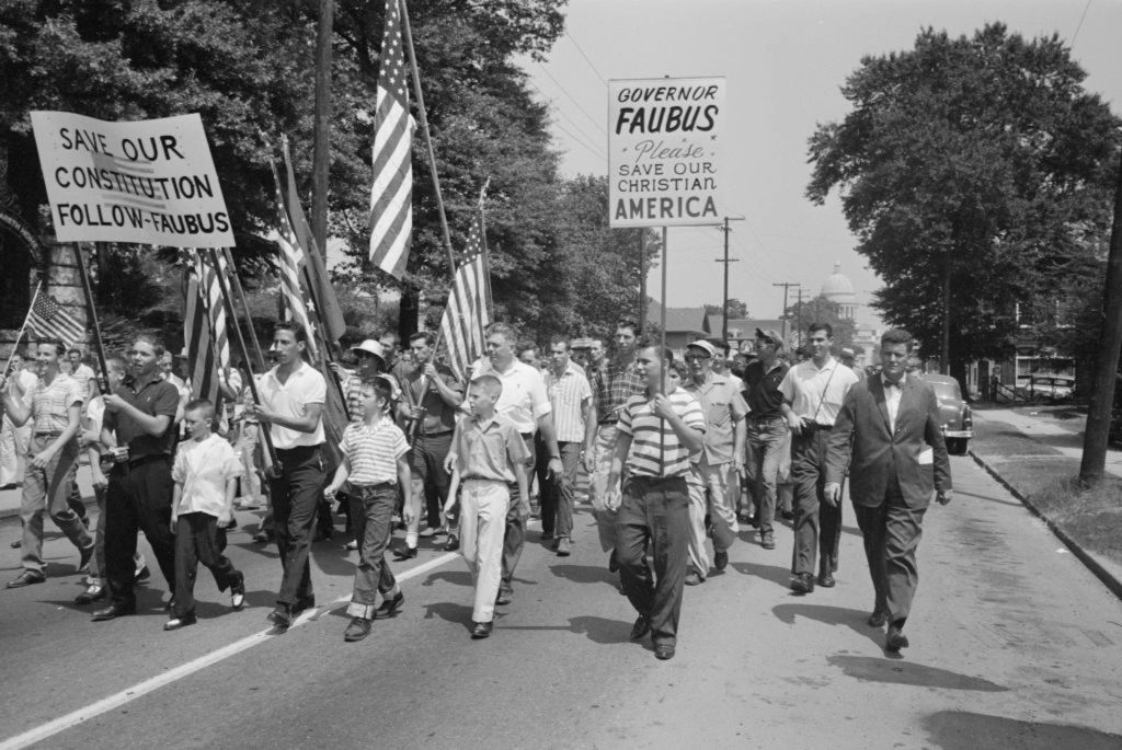 A black-and-white photo of men and boys marching down a street, holding placards and American flags