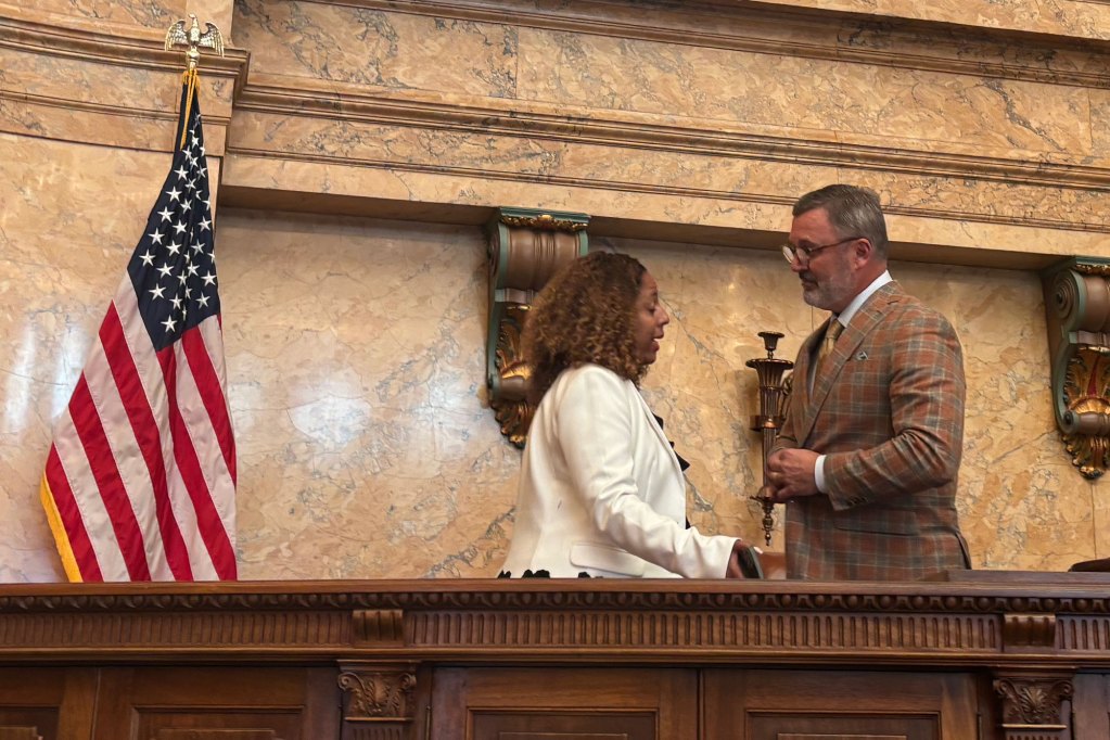 A woman and a man talk while standing on the dais of the Mississippi House floor.