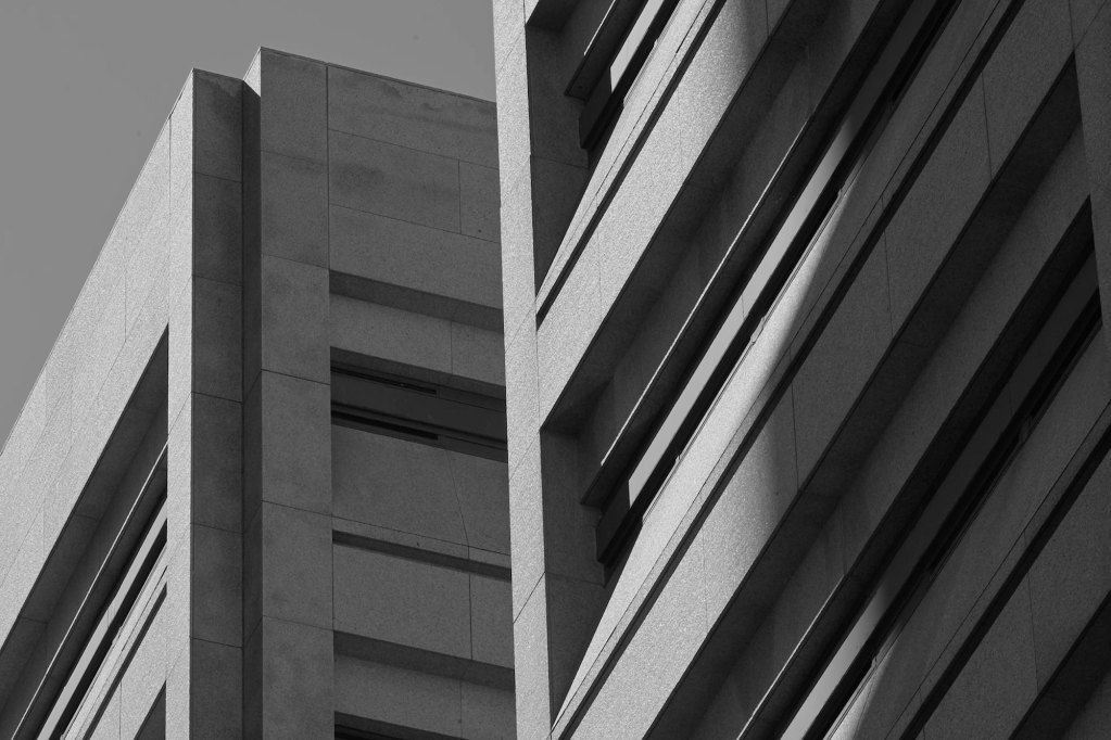 A black-and-white photo shows a partial shadow over a multi-story jail complex with thin, horizontal windows.