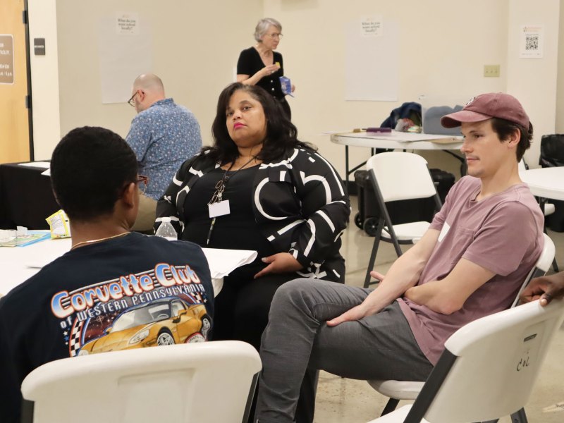 Three people sit around a circular table and talk