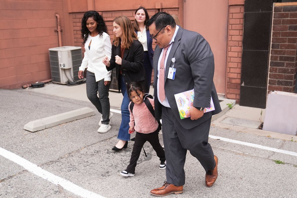 A 4 year old girl is being walked by an adult paralegal outside of a building as family walks behind them