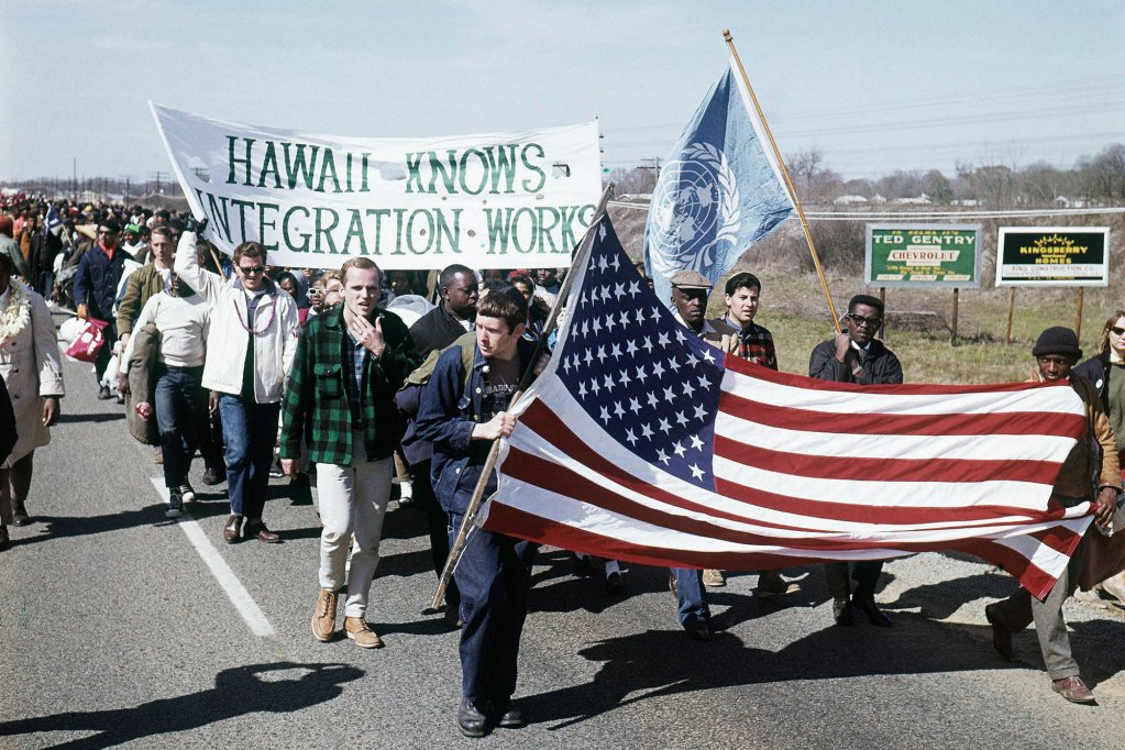 A multi-racial group of supporters march with signs like "Hawaii Knows Integration Works"