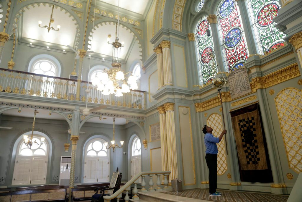 A man in a blue shirt holds up a long tool inside an airy room with stained glass windows