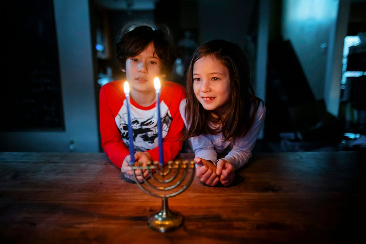 Two children look at a menorah with two lit candles