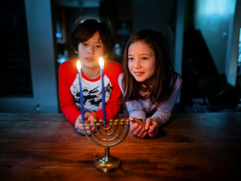 Two children look at a menorah with two lit candles