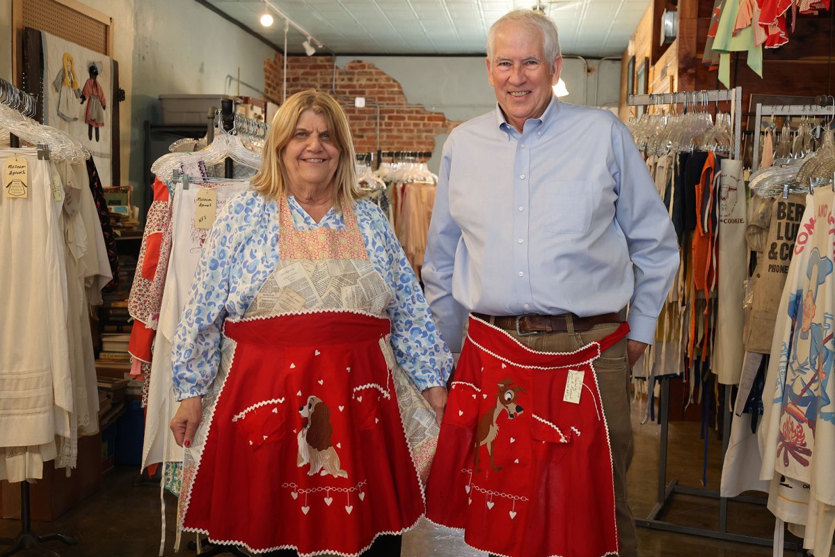 A man and woman both in blue shirts have red aprons around their waist