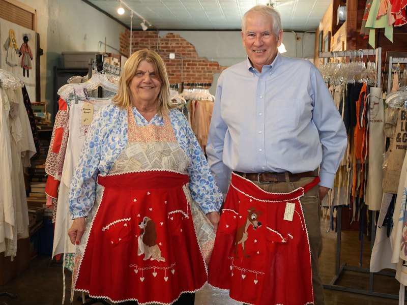 A man and woman both in blue shirts have red aprons around their waist