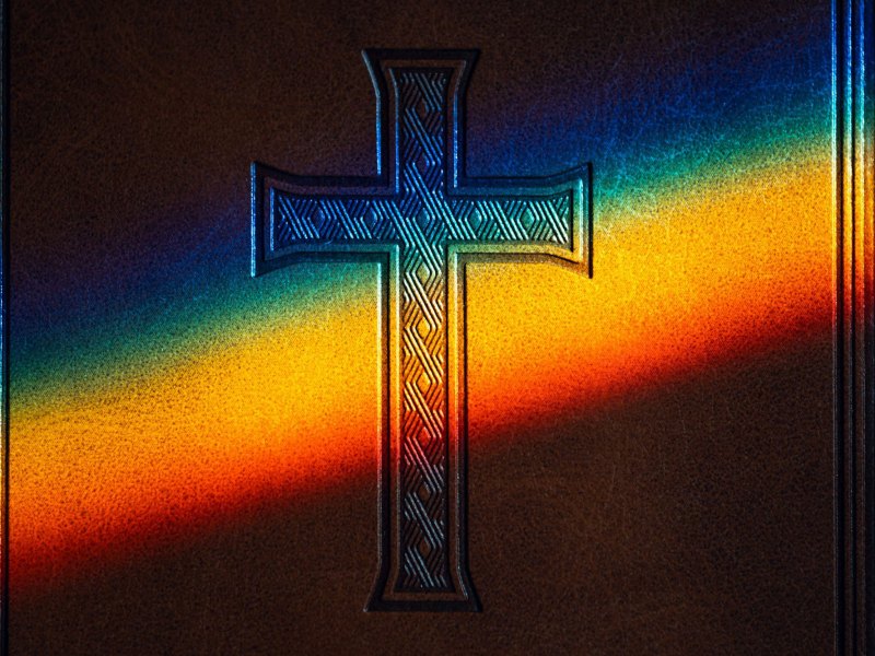 A book with a cross embeded in leather is lit with a rainbow from a prism