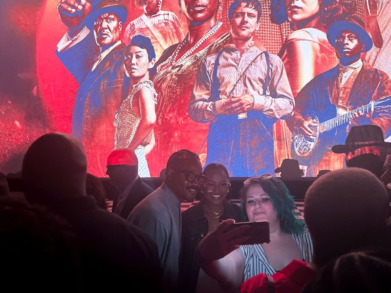 Moviegoer takes picture with two people in front of a red and blue colorful projected poster