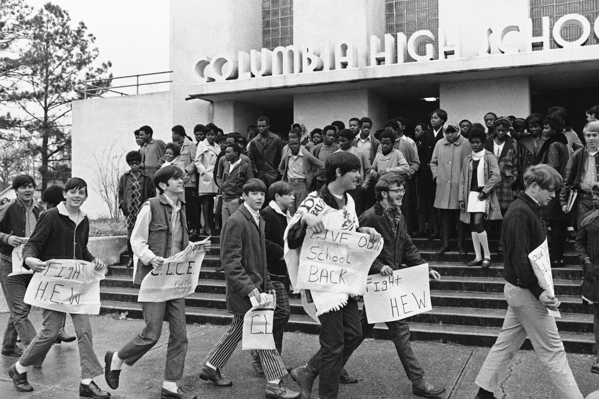 White students walk in front of black Columbia High School students with signs like “Give our school back”