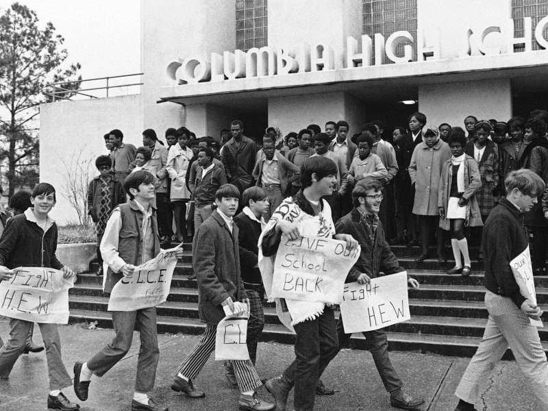 White students walk in front of black Columbia High School students with signs like “Give our school back”