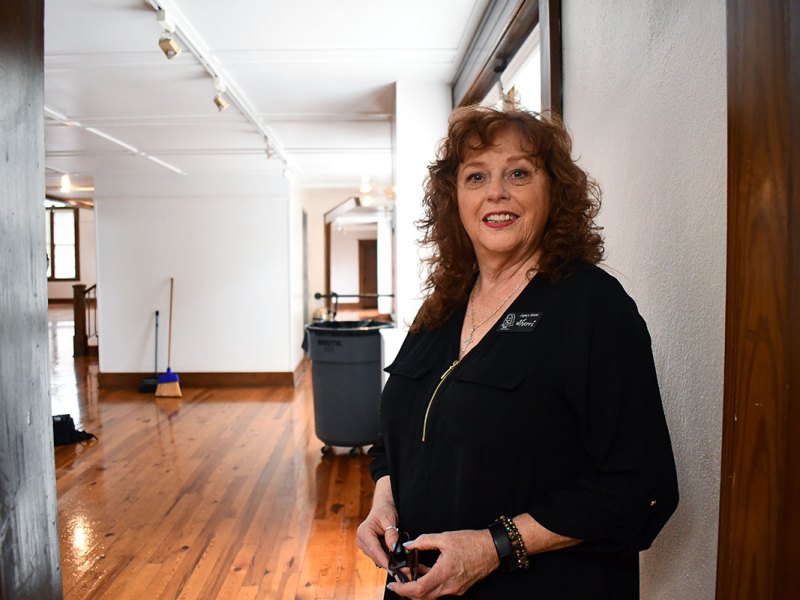 A woman dressed in black stands inside a hallway that's white walls and wooden trim