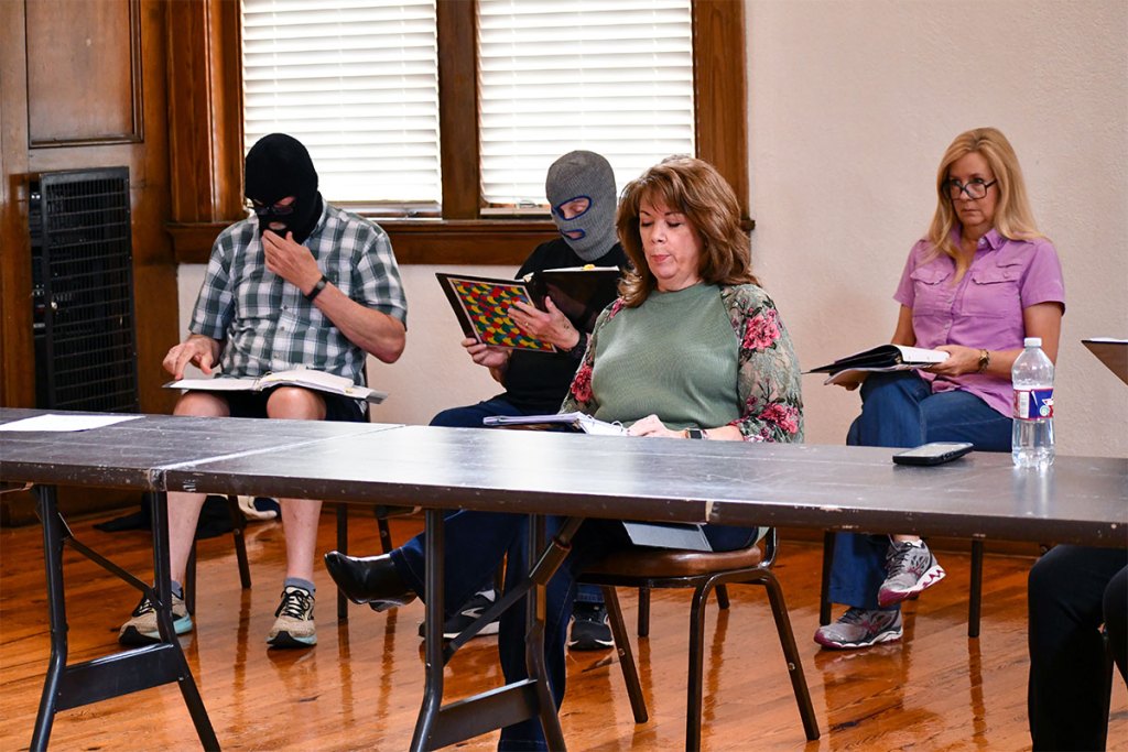 Four people are seen sitting in chairs and looking at folders in their hands