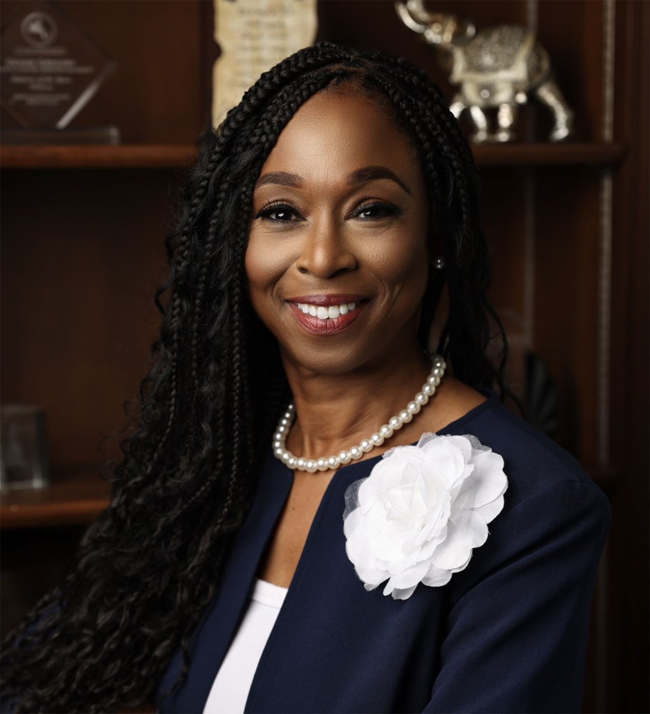 A woman wearing a navy cardigan with a white flower on the sweater and pearls around her neck