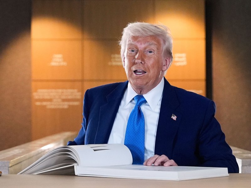 Donald Trump stands behind a desk to sign a large guest book