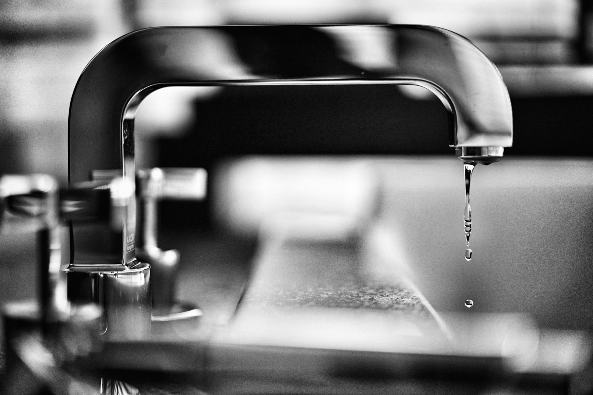 A black and white photo of a indoor water faucet dripping water