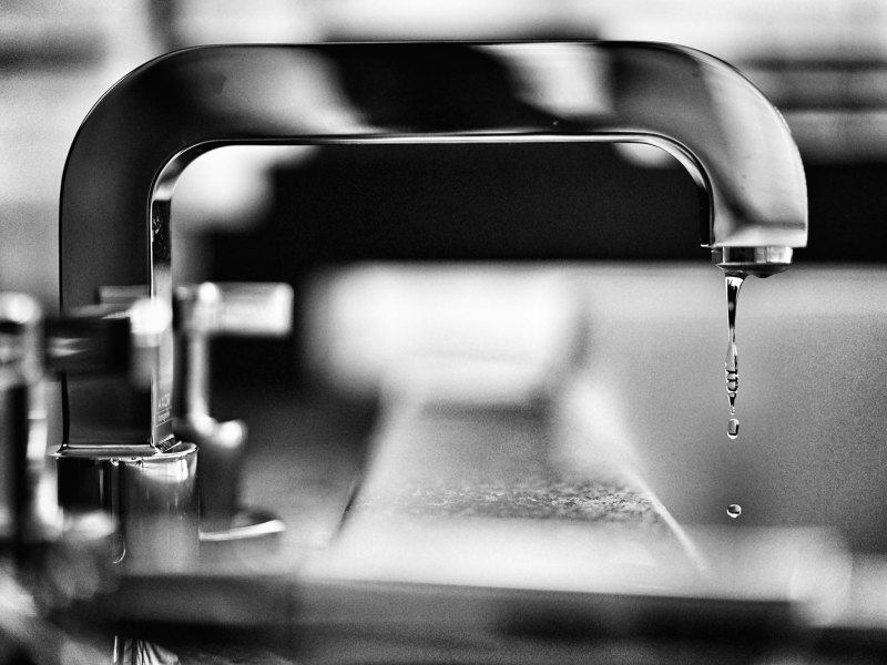 A black and white photo of a indoor water faucet dripping water
