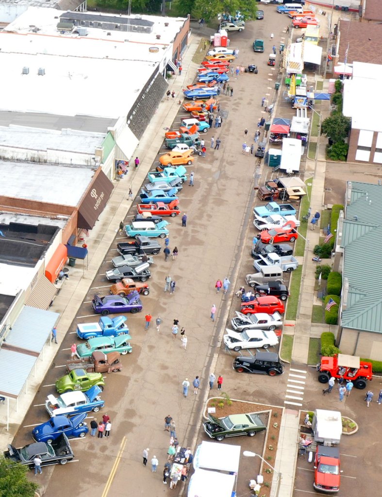 An aerial view of a city street lined with vintage cars on display