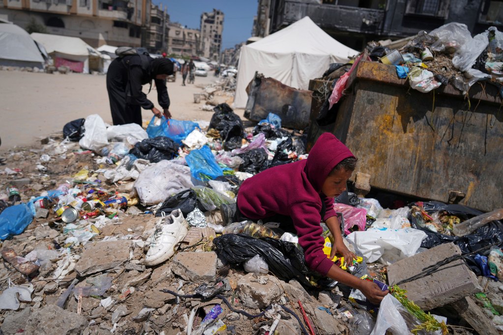 a child a woman sort through a garbage pile in war torn Gaza, searching for leftover food
