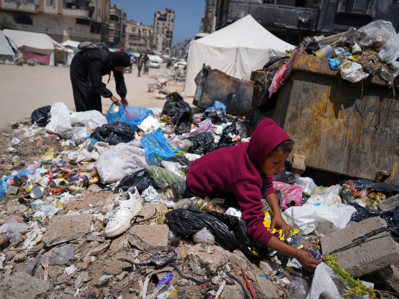 a child a woman sort through a garbage pile in war torn Gaza, searching for leftover food