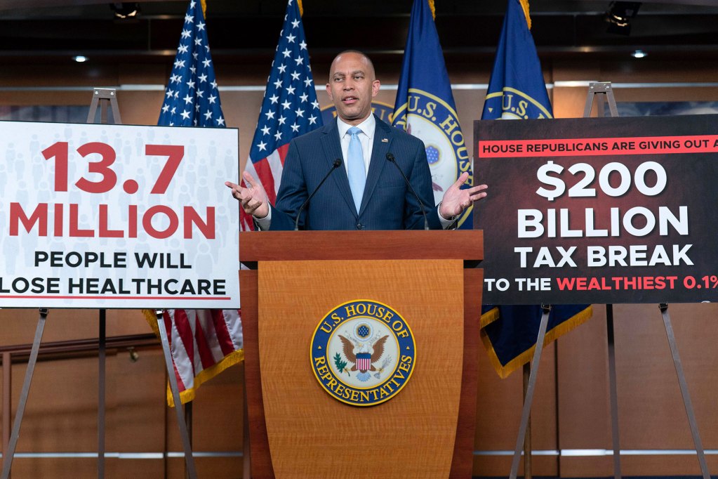 Hakeem Jeffries speaks on stage with signs that read "13.7 Million people will lose healthcare" and "$200 Billion tax break to the wealthiest 0.1%"