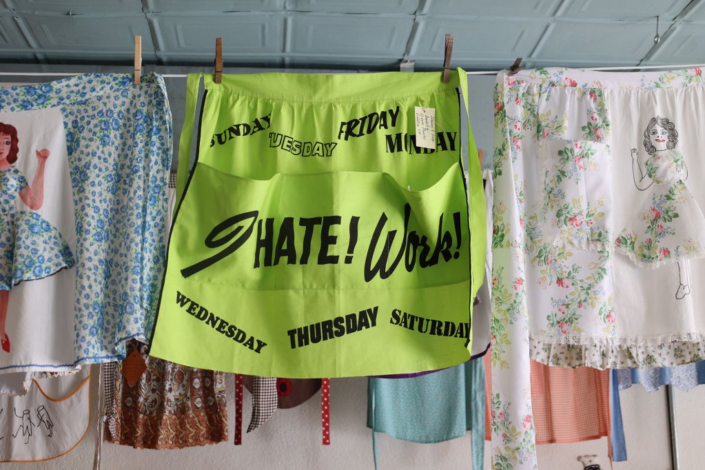 A neon apron with the words I hate work written on it along with the days of the week