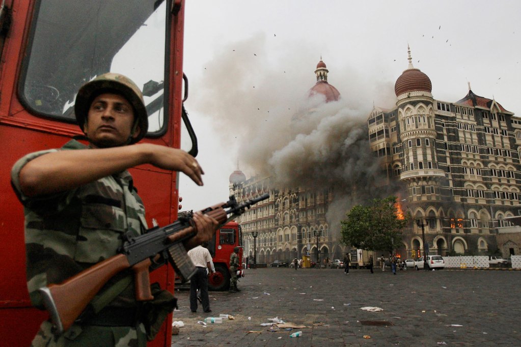 An Indian soldier takes cover as the Taj Mahal hotel burns during a gun battle
