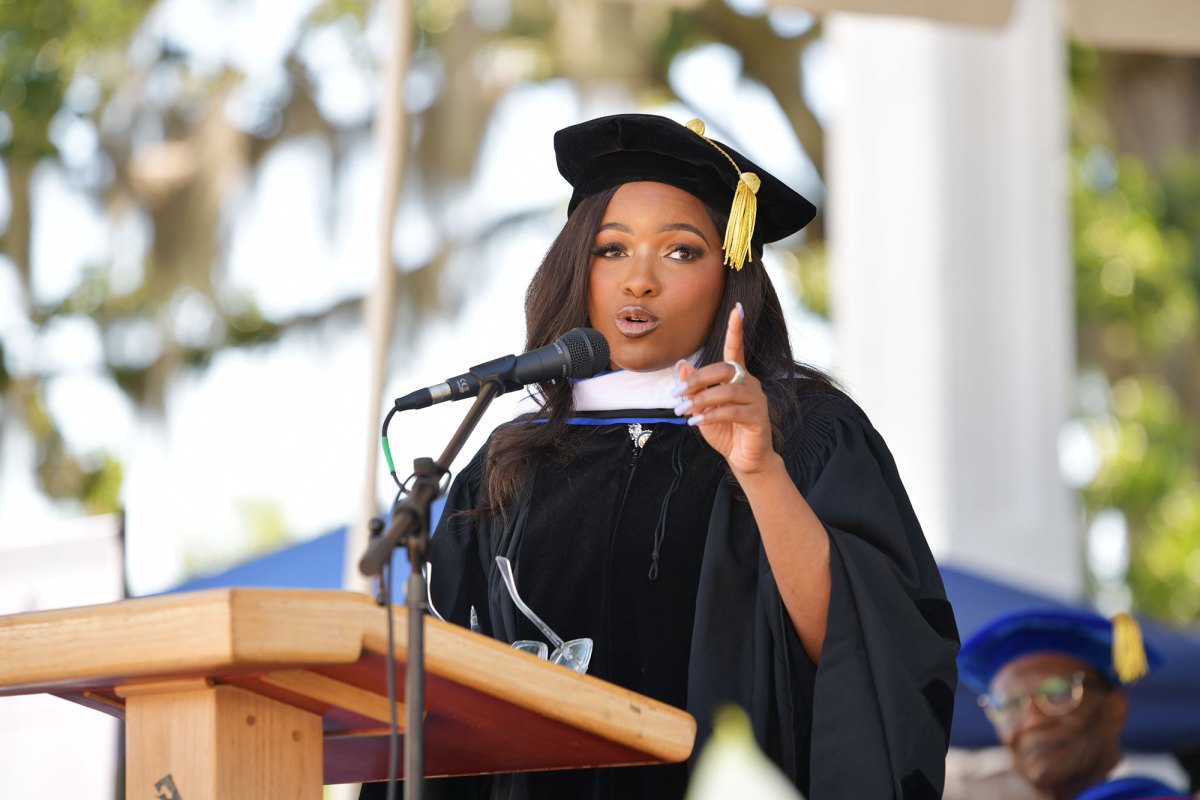 A woman wearing a black cap and gown speaking at a podium