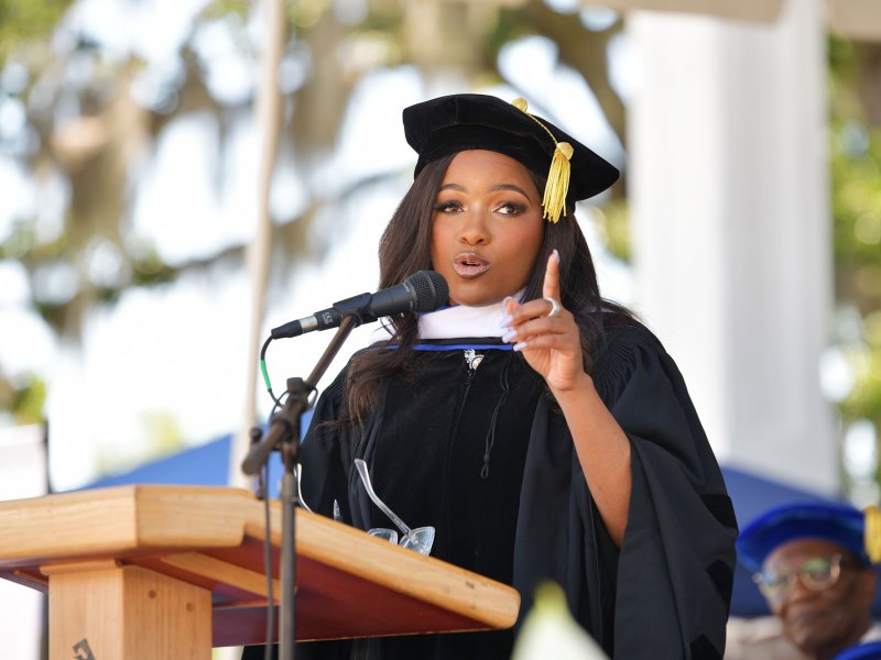 A woman wearing a black cap and gown speaking at a podium