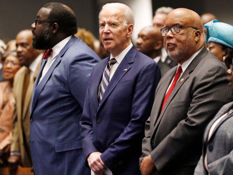 A row of men in suits including Joe Biden and Bennie Thompson stand and attend a church service