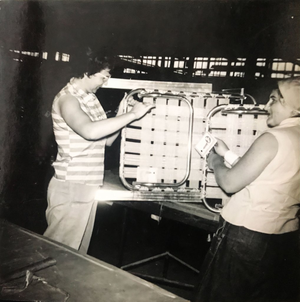 A black and white photo of two women holding folding gardening chairs