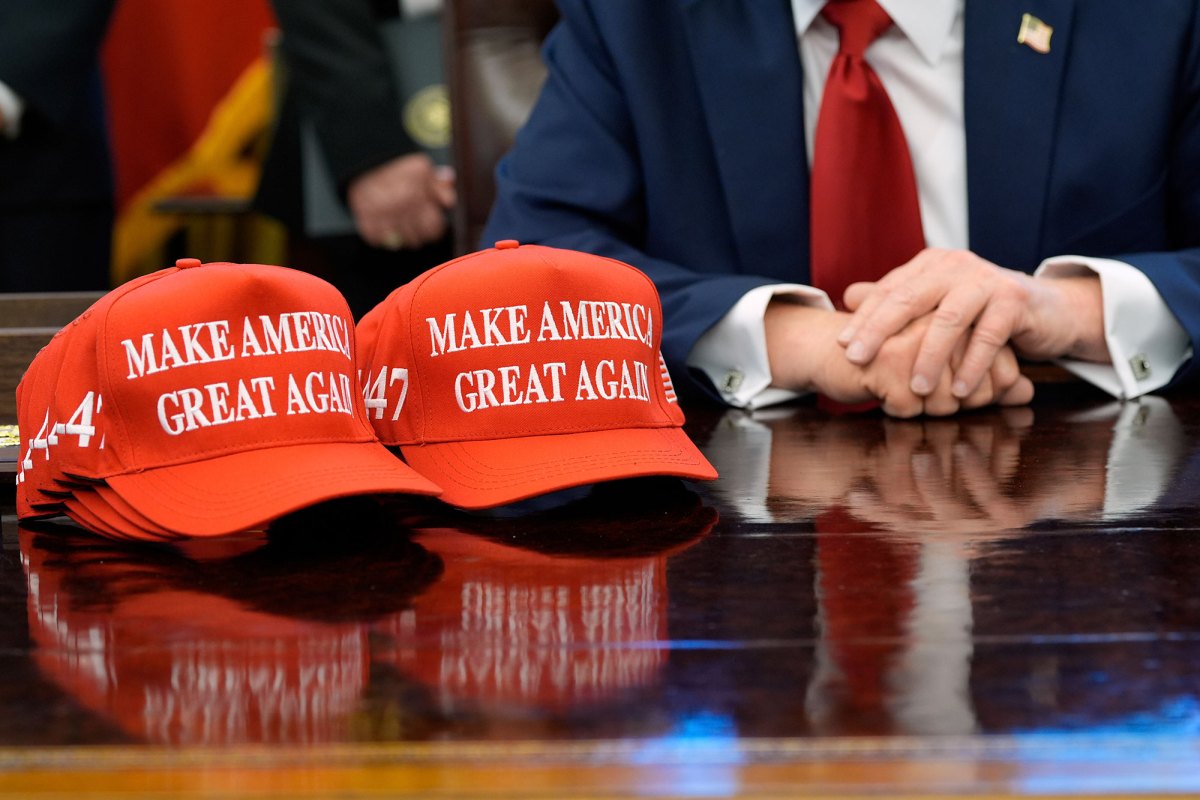 Red hats that read “Make America Great Again” sit beside President Donald Trump on his desk