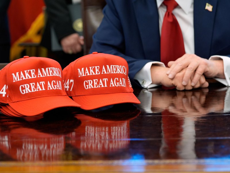 Red hats that read “Make America Great Again” sit beside President Donald Trump on his desk