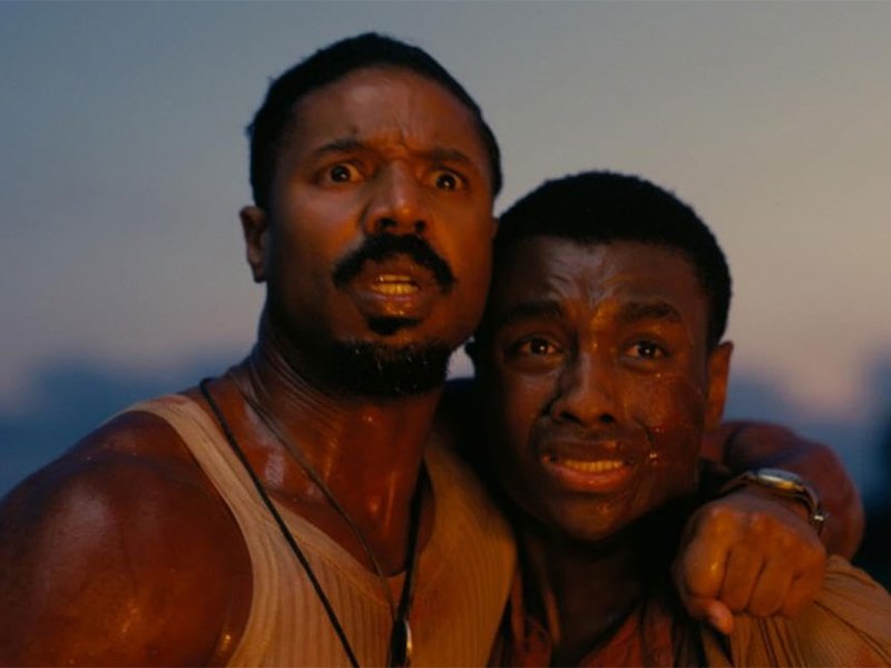 Two men hold each other close and look at something, crying