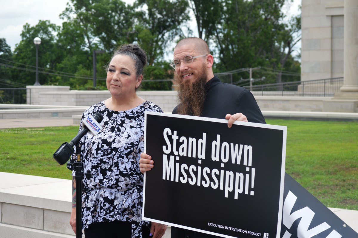 A man and a woman hold a black sign that reads Stand Down Mississippi!