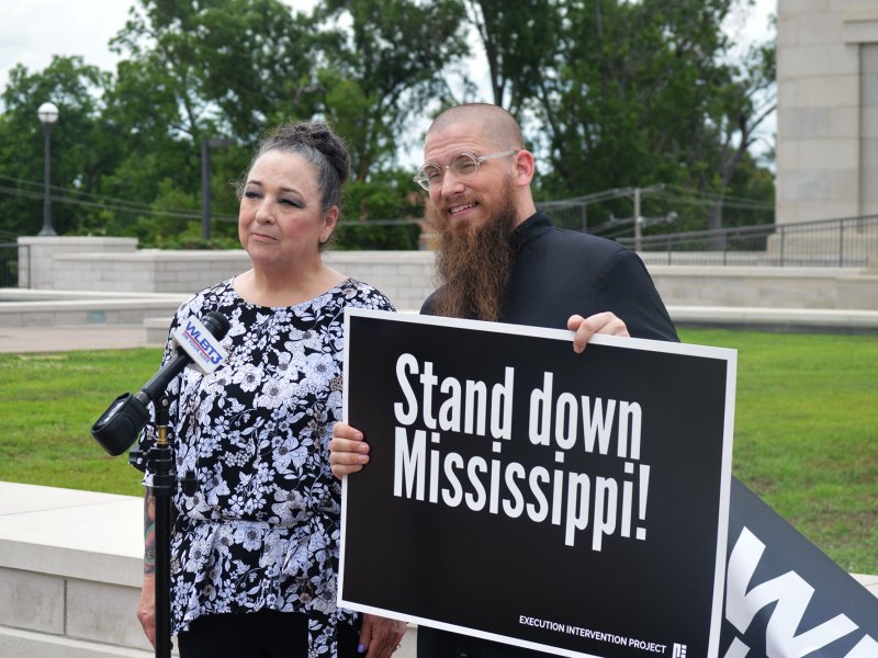 A man and a woman hold a black sign that reads Stand Down Mississippi!