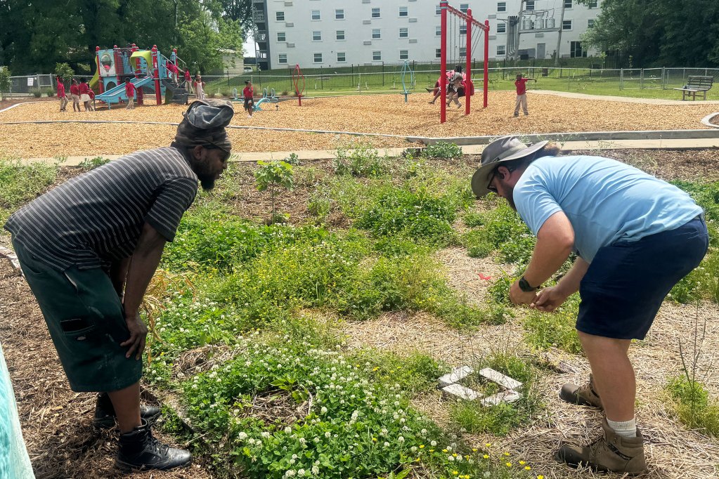 Two men standing in a garden and behind them a playground with children wearing red