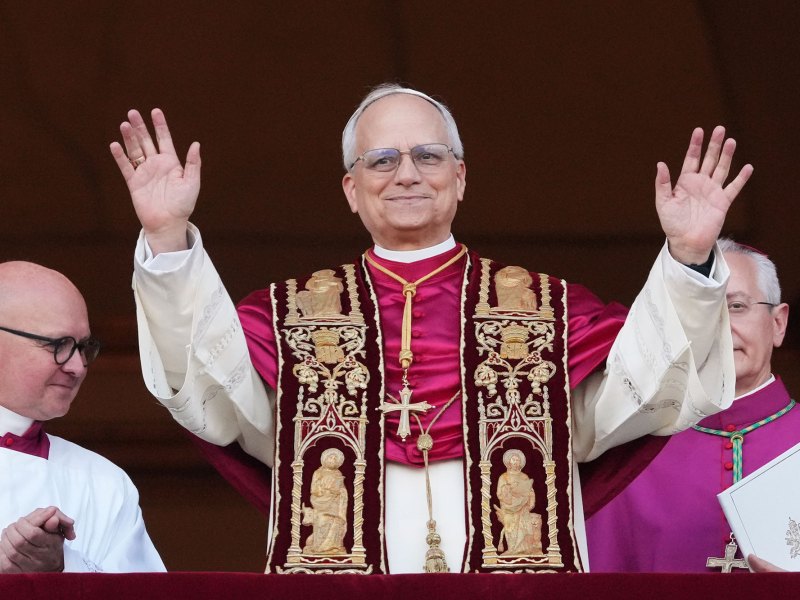 Pope Leo XIV smiles and waves from a balcony to the crowd below