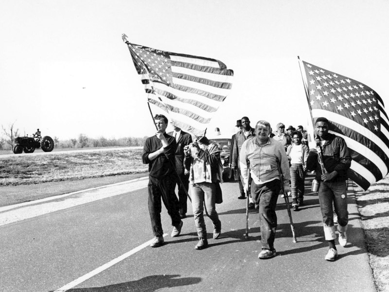 A black and white photo of people marching down a road, carrying U.S. flags