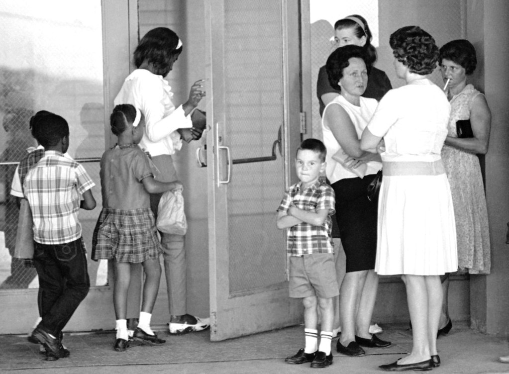 A group of African American students, left, enter the school as a group of white mothers wait at the entrance.