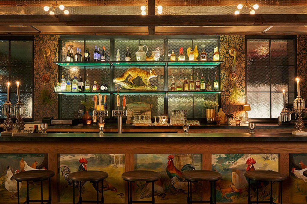 A bar that features rooster iconography and a statue of a fox amid shelves of liquor bottles
