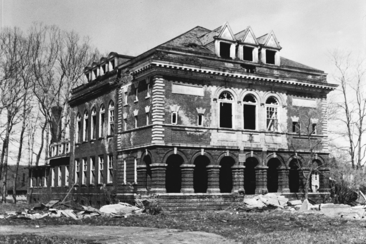 An old black and white photo of a large three story house in disrepair