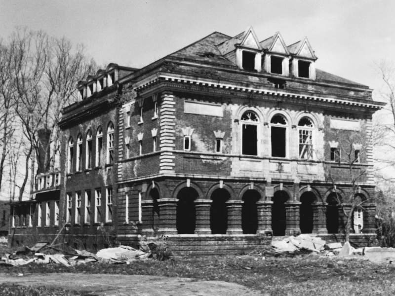 An old black and white photo of a large three story house in disrepair