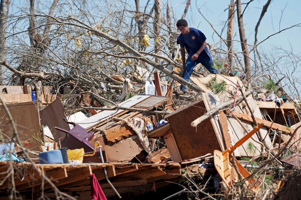 A teen walks over a huge pile of household tornado debris