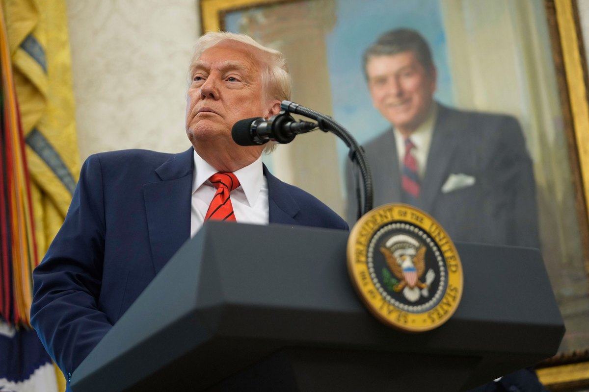 President Donald Trump speaks behind a podium, a portrait of President Regan behind him