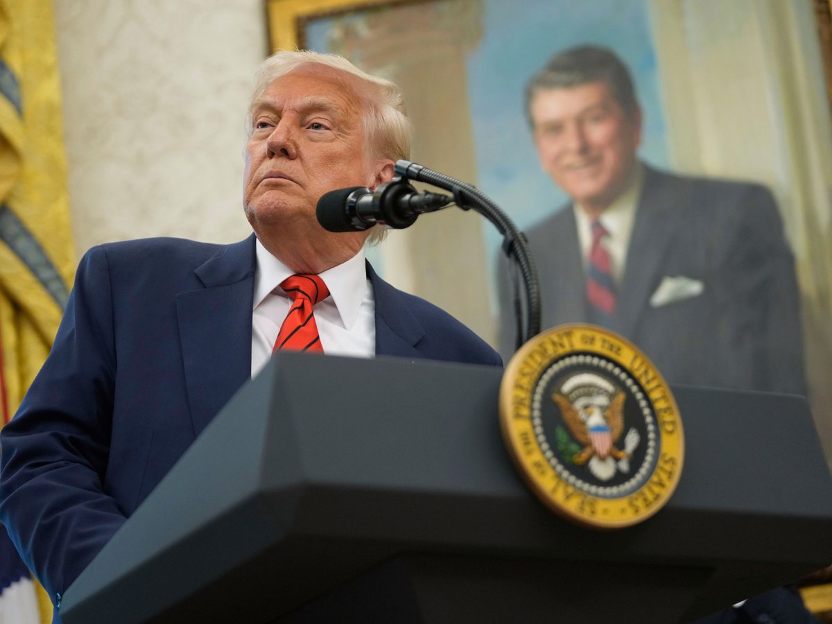President Donald Trump speaks behind a podium, a portrait of President Regan behind him