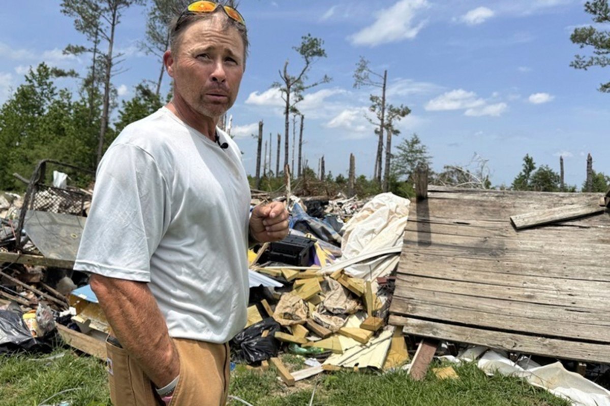 Man in grey shirt and khaki's stand in front of a pile of debris in an open field